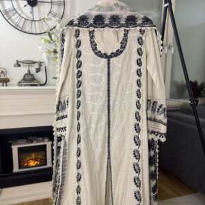 A white embroidered 3 piece suit hanging on a rack with a decorative background.