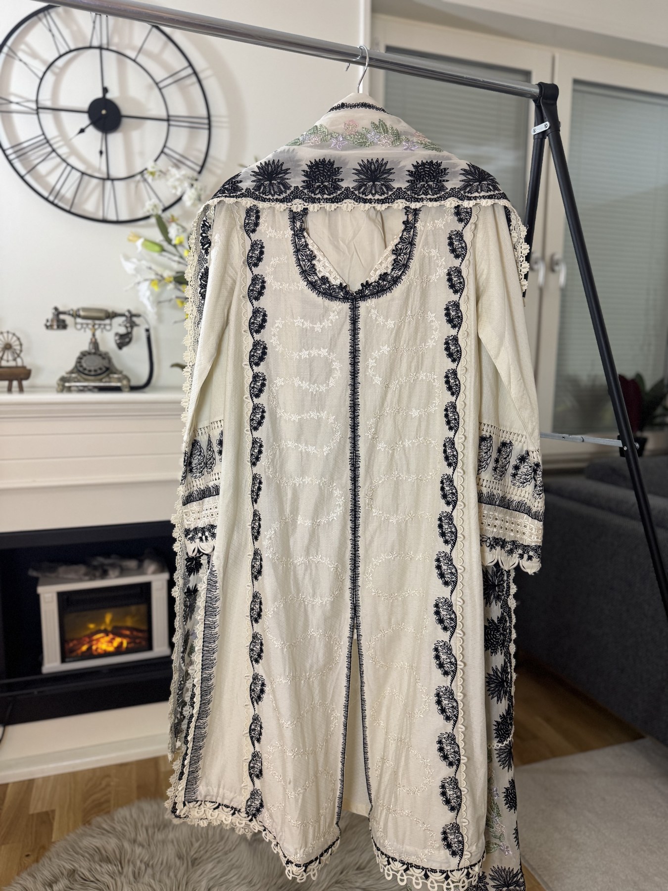 A white embroidered 3 piece suit hanging on a rack with a decorative background.